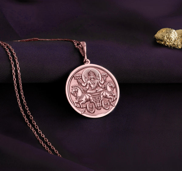 rose gold plated Surya necklace featuring a detailed pendant of the Hindu sun god, Surya, with intricate solar rays design. Crafted with rose gold plating, this mythological-inspired jewelry piece symbolizes light, energy, and divine protection. Ideal for those seeking Hindu cultural jewelry or a unique sun-themed accessory. The pendant depicts Surya riding his chariot, pulled by seven horses, with lotus flowers in hand, radiating warmth and enlightenment."