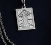 The Tower tarot card silver boho chic pendant necklace , depicted in a striking silver color features a tall, imposing structure being struck by highlighting the crumbling tower as it tilts precariously. Two figures are shown falling from the structure, symbolizing sudden upheaval or chaos. The background is often minimal, allowing the vivid silver tones to emphasize the tower's destruction and the sense of unexpected change or revelation it represents.
