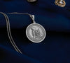 Sterling silver Buddha pendant necklace displaying a serene meditation scene. This detailed circular medallion captures Buddha in contemplative pose with head resting on hand, surrounded by an ornately engraved border. The pendant features meticulous craftsmanship with an oxidized finish highlighting the peaceful expression and flowing robes. Displayed on white silk fabric with a matching silver chain, this spiritual jewelry piece symbolizes tranquility, mindfulness