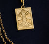 The Tower tarot cardboho chic pendant necklace , depicted in a striking gold color features a tall, imposing structure being struck by highlighting the crumbling tower as it tilts precariously. Two figures are shown falling from the structure, symbolizing sudden upheaval or chaos. The background is often minimal, allowing the vivid gold tones to emphasize the tower's destruction and the sense of unexpected change or revelation it represents.