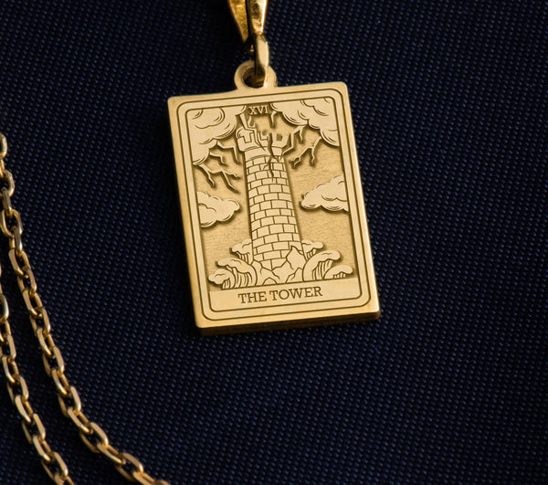 The Tower tarot cardboho chic pendant necklace , depicted in a striking gold color features a tall, imposing structure being struck by highlighting the crumbling tower as it tilts precariously. Two figures are shown falling from the structure, symbolizing sudden upheaval or chaos. The background is often minimal, allowing the vivid gold tones to emphasize the tower's destruction and the sense of unexpected change or revelation it represents.