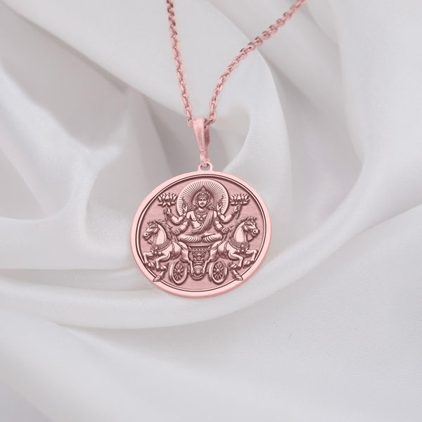 rose gold plated Surya necklace featuring a detailed pendant of the Hindu sun god, Surya, with intricate solar rays design. Crafted with rose gold plating, this mythological-inspired jewelry piece symbolizes light, energy, and divine protection. Ideal for those seeking Hindu cultural jewelry or a unique sun-themed accessory. The pendant depicts Surya riding his chariot, pulled by seven horses, with lotus flowers in hand, radiating warmth and enlightenment."
