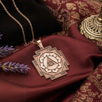 The 925 sterling silver Ganesh Yantra necklace, a spiritual amulet for good luck and success, is displayed on red silk with lavender. The light catches the detailed sacred geometry of the Remover of Obstacles, emphasizing its handcrafted quality. This powerful talisman makes a meaningful graduation or new job gift, with options in 14k gold and rose gold plated.