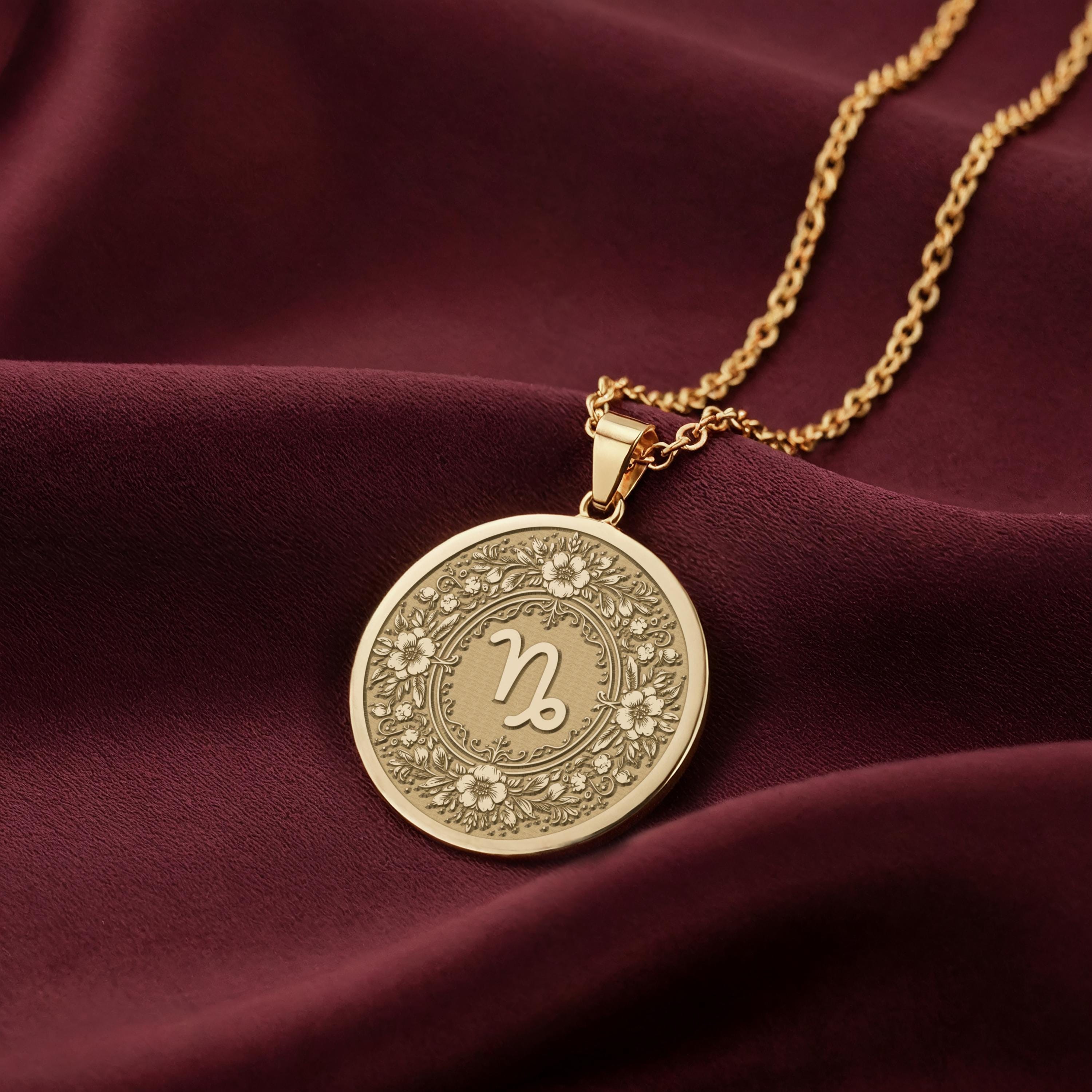 14K Solid Gold Capricorn Zodiac Medallion featuring goat horn symbol surrounded by intricate floral botanical patterns and decorative elements. Detailed astrology coin pendant with celestial symbolism. Luxury Capricorn jewelry representing ambitious energy and earthly strength
