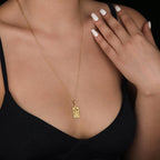 The Tower tarot card  boho chic pendant necklace , depicted in a striking gold color features a tall, imposing structure being struck by highlighting the crumbling tower as it tilts precariously. Two figures are shown falling from the structure, symbolizing sudden upheaval or chaos. The background is often minimal, allowing the vivid gold tones to emphasize the tower's destruction and the sense of unexpected change or revelation it represents.