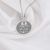 Buddha figure seated in meditative lotus pose (Padmasana) upon a blooming lotus flower base. The bright, cool shine of the polished 925 sterling silver beautifully accentuates the detailed lines of the central deity and the surrounding ornate floral mandala-style patterns filling the circular frame.
