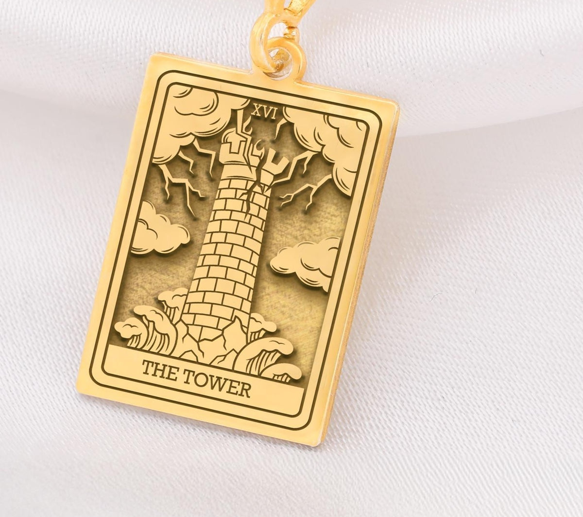 The Tower tarot card  boho chic pendant necklace , depicted in a striking gold color features a tall, imposing structure being struck by highlighting the crumbling tower as it tilts precariously. Two figures are shown falling from the structure, symbolizing sudden upheaval or chaos. The background is often minimal, allowing the vivid gold tones to emphasize the tower's destruction and the sense of unexpected change or revelation it represents.