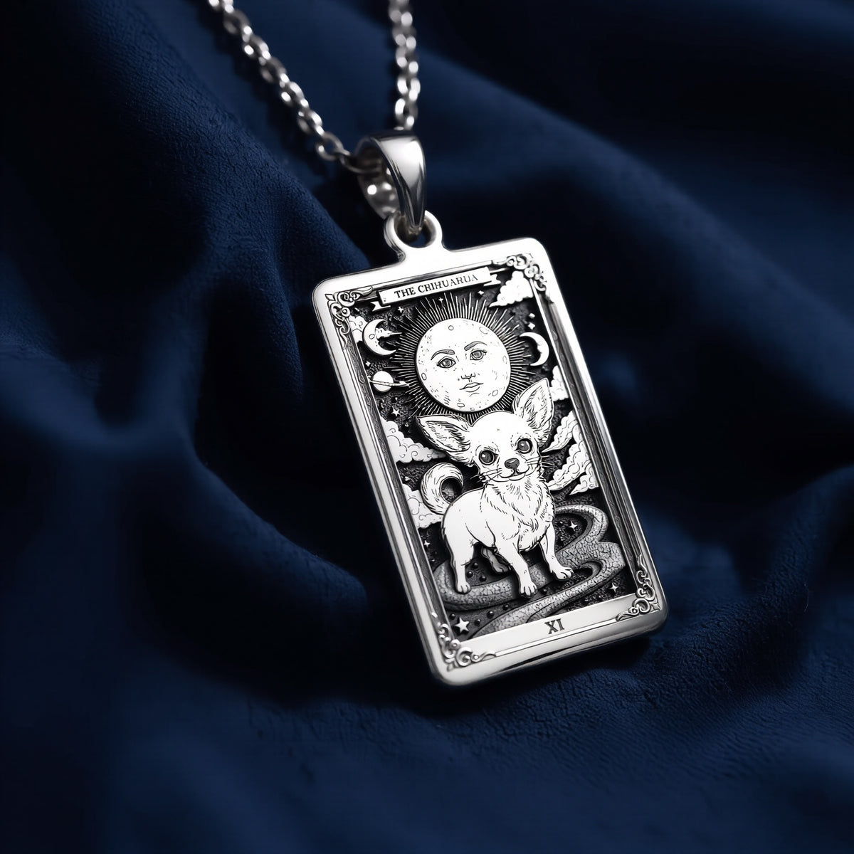 Rectangular sterling silver pendant featuring an engraved Chihuahua tarot card design with celestial moon, stars, and Roman numeral XI; displayed on a fine link chain against dark blue fabric.