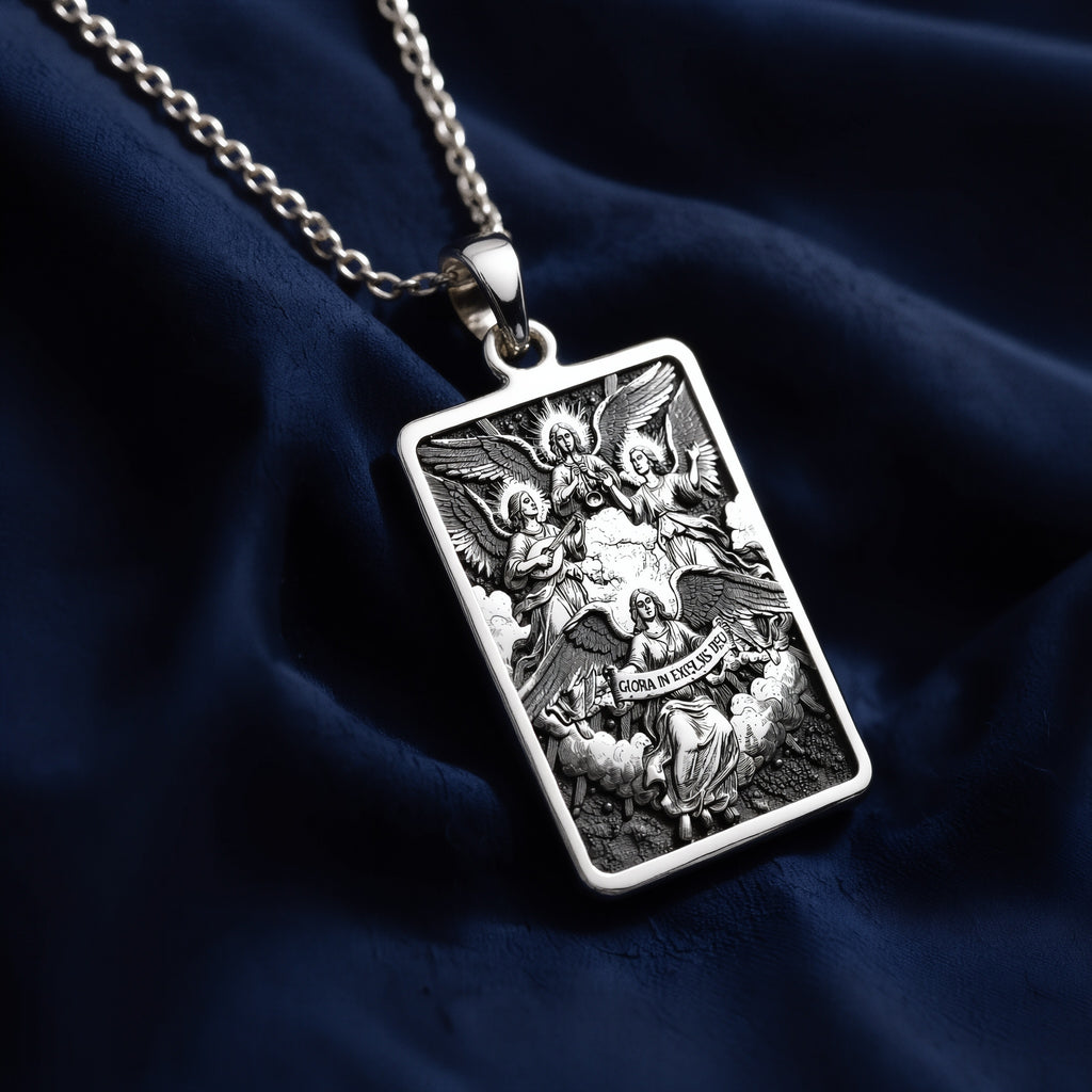 Rectangular sterling silver pendant necklace featuring a detailed relief engraving of four angels playing musical instruments with the Latin inscription "Gloria in Excelsis Deo," suspended from a polished cable chain on deep blue fabric.