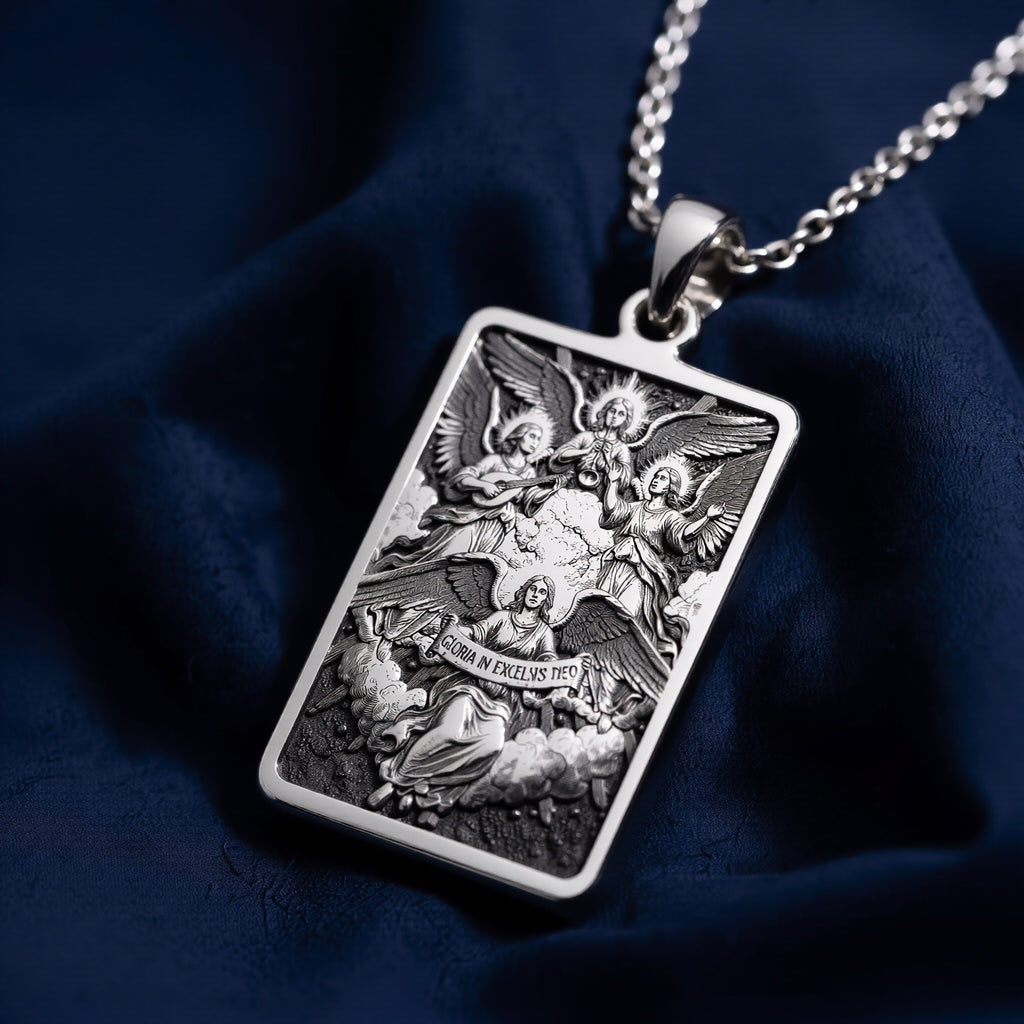 Silver rectangular pendant with an engraved relief design of angels and figures and Latin text. This piece is suspended from a silver chain and rests on a dark surface.