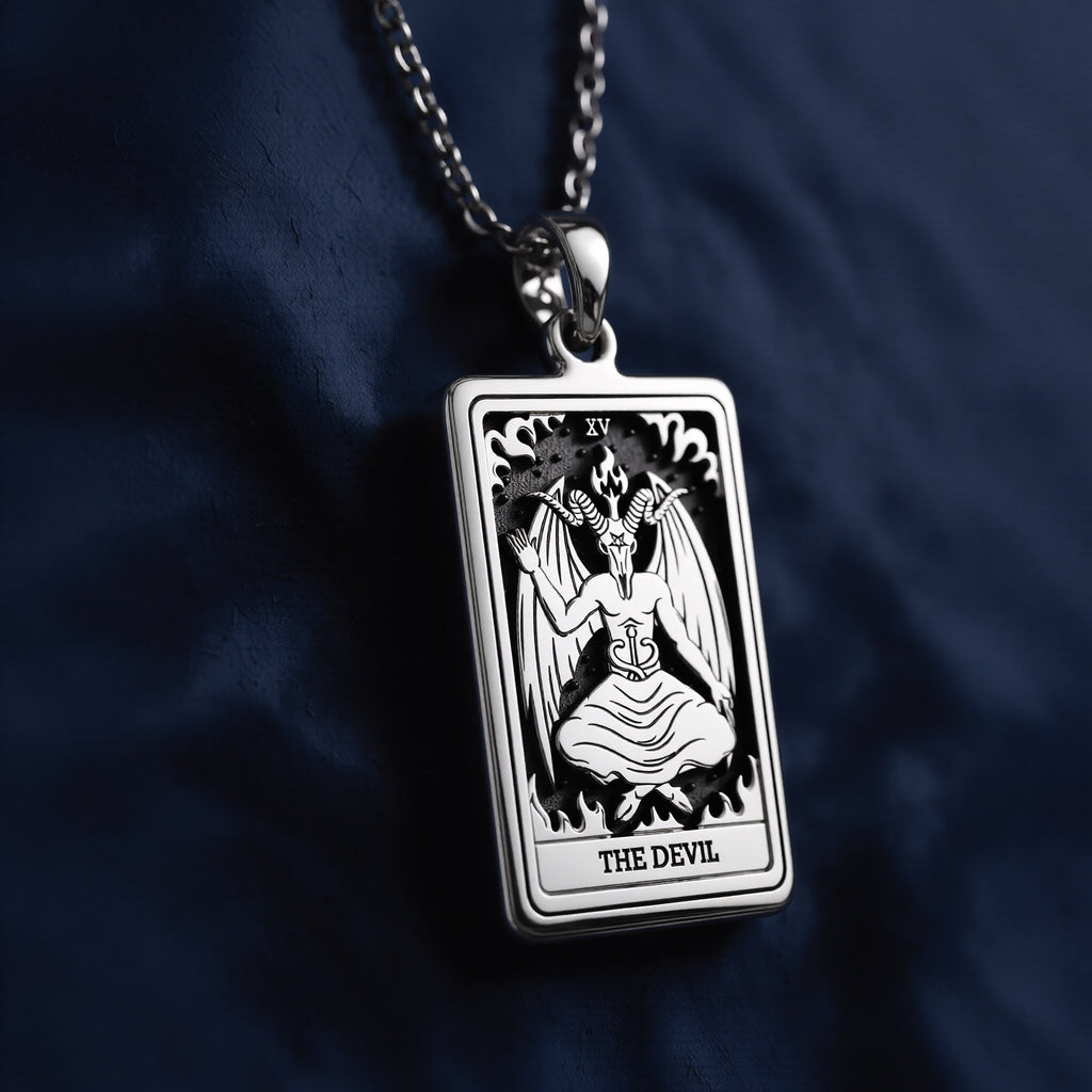 Rectangular sterling silver pendant necklace featuring an engraved Rider Waite Tarot "The Devil" card (XV) with a winged figure, flames, and bold lettering, suspended from a polished link chain against navy fabric.