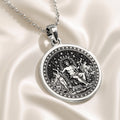 Silver circular pendant featuring a detailed classical scene with figures, presented in a silver tone. The pendant hangs from a silver chain and is viewed from the front.