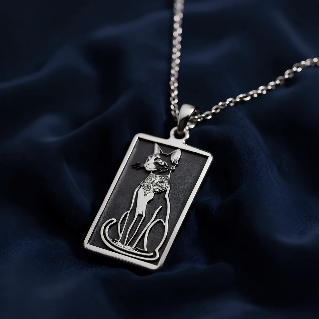 Silver pendant necklace featuring a stylized cat head design with intricate details, shown from a slight angle. The chain is visible, and the surface has a polished finish.