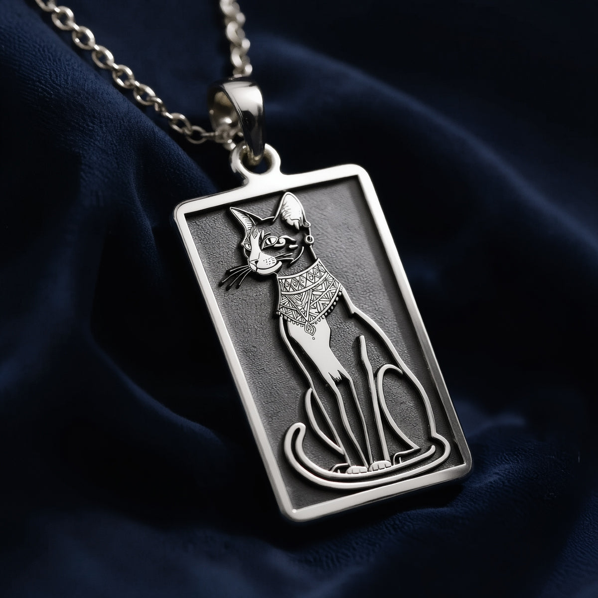 Silver rectangular pendant featuring an etched outline design of a cat. This necklace is attached to a silver chain and presented on a dark surface.