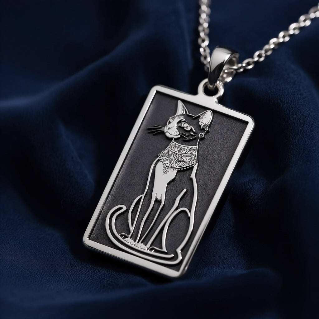 Silver rectangular pendant with an engraved outline design of a cat. The pendant hangs from a silver chain, displayed alongside various gemstones.