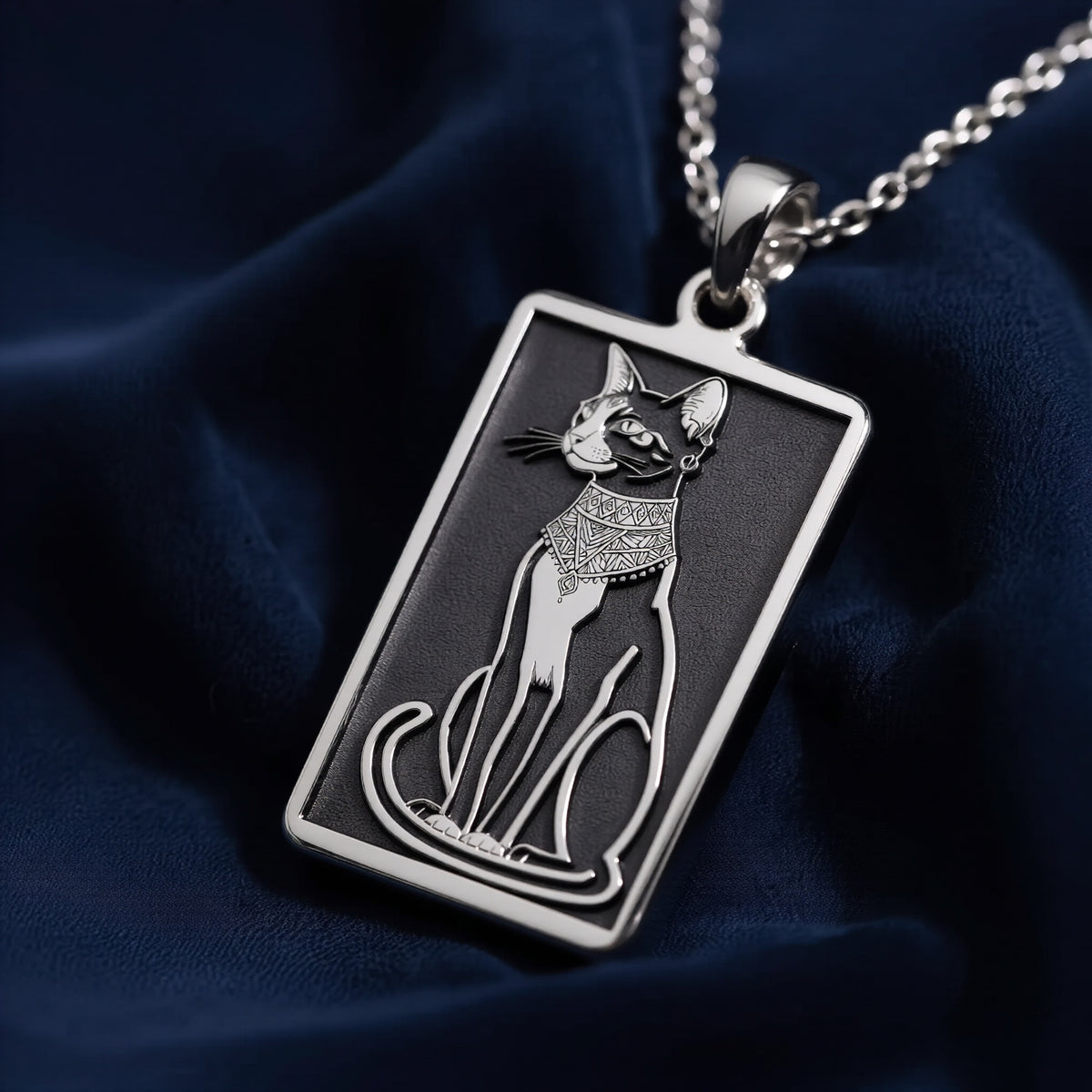 Silver rectangular pendant with an engraved outline design of a cat. The pendant hangs from a silver chain, displayed alongside various gemstones.