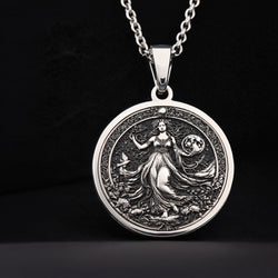Silver pendant necklace featuring an intricate design of a female figure surrounded by foliage, with a detailed surface finish. The pendant is circular and hangs from a delicate chain.