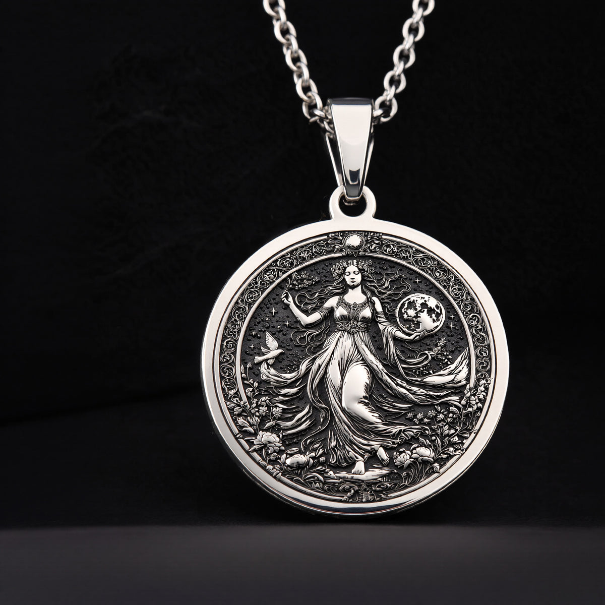 Silver pendant necklace featuring an intricate design of a female figure surrounded by foliage, with a detailed surface finish. The pendant is circular and hangs from a delicate chain.