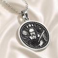 Silver pendant featuring a detailed design of Galileo looking through a telescope, circular shape with an engraved surface finish. The pendant is displayed resting on a dark, textured fabric