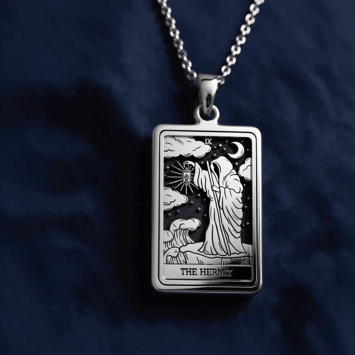 Rectangular sterling silver pendant featuring an engraved depiction of The Hermit tarot card, showing a robed figure holding a lantern beneath a crescent moon and stars with clouds and waves.