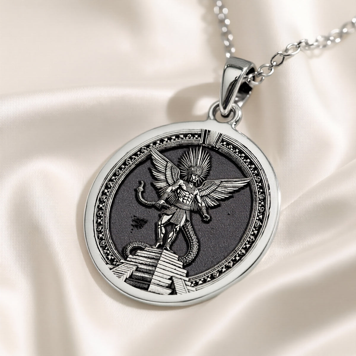 Silver circular pendant showcasing a detailed Aztec winged figure with feathered wings and a serpentine base. The piece hangs from a silver chain