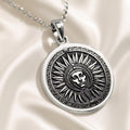 Silver circular pendant featuring an engraved sun motif with facial details and radiating lines. This pendant hangs from a silver chain against a blue background.