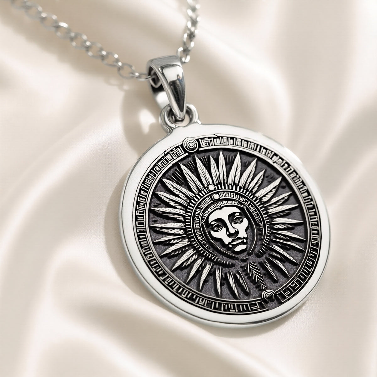 Silver circular pendant featuring an engraved sun motif with facial details and radiating lines. This pendant hangs from a silver chain against a blue background.