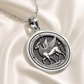Silver-toned circular pendant featuring an ancient Egyptian winged creature motif standing on a base, detailed with surrounding text and borders. The pendant is attached to a silver chain and displayed against a dark background