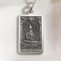 Memento Docendo Tarot Pendant necklace. Rectangular sterling silver pendant with raised skull over open book and ornate scrollwork border.