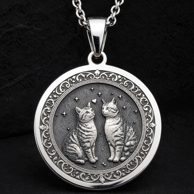Silver pendant necklace featuring a circular design with two stylized cats facing each other within an ornate border. The metal has a polished finish and is displayed against a dark background.