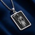 Silver pendant necklace featuring a detailed framed depiction of a hooded figure with a scythe and skulls. The pendant is presented on dark fabric alongside faceted gemstones.