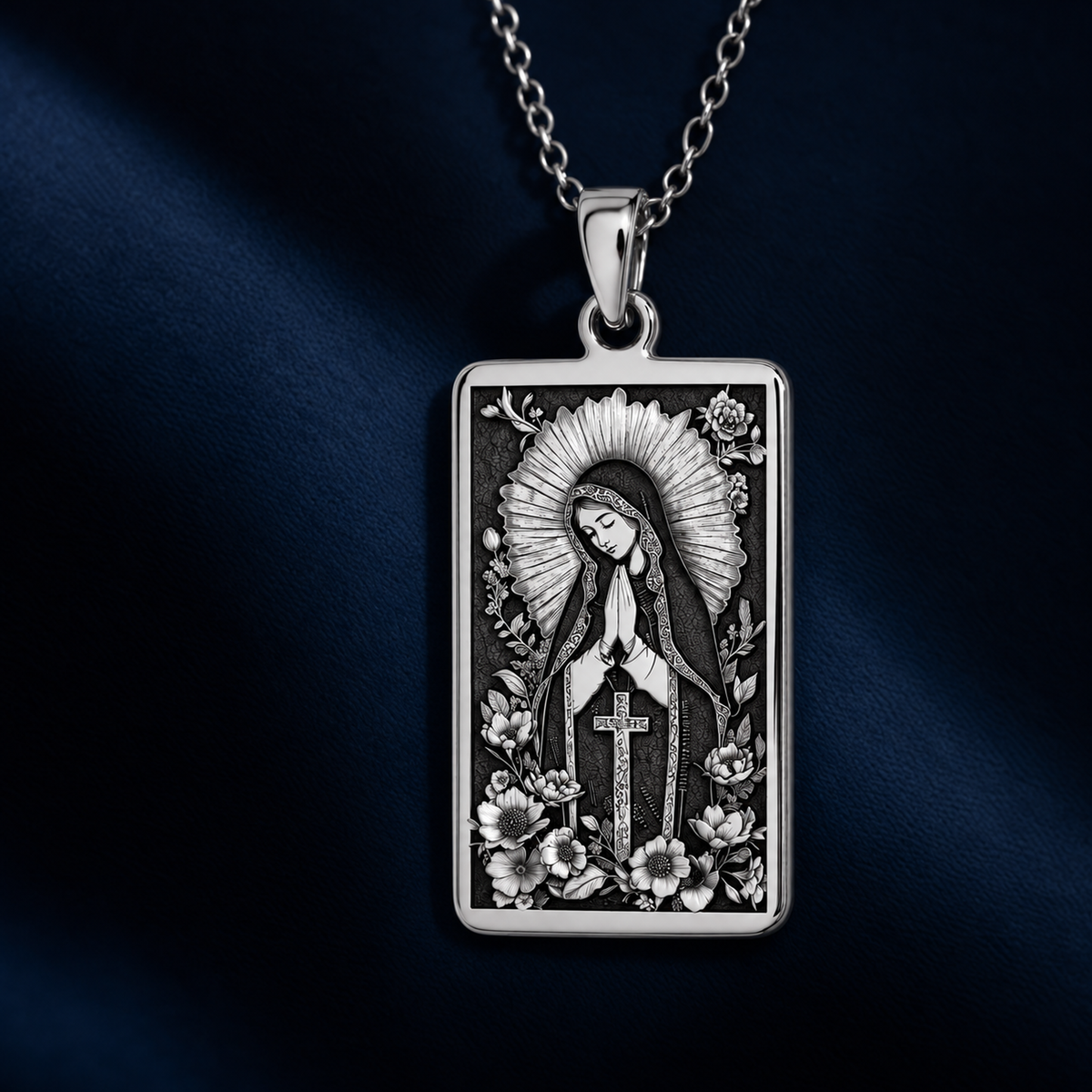 Silver plated rectangular pendant necklace featuring an ornate design of a figure framed by floral elements. The pendant is attached to a silver-toned chain and displayed on a black velvet background with scattered gemstones.