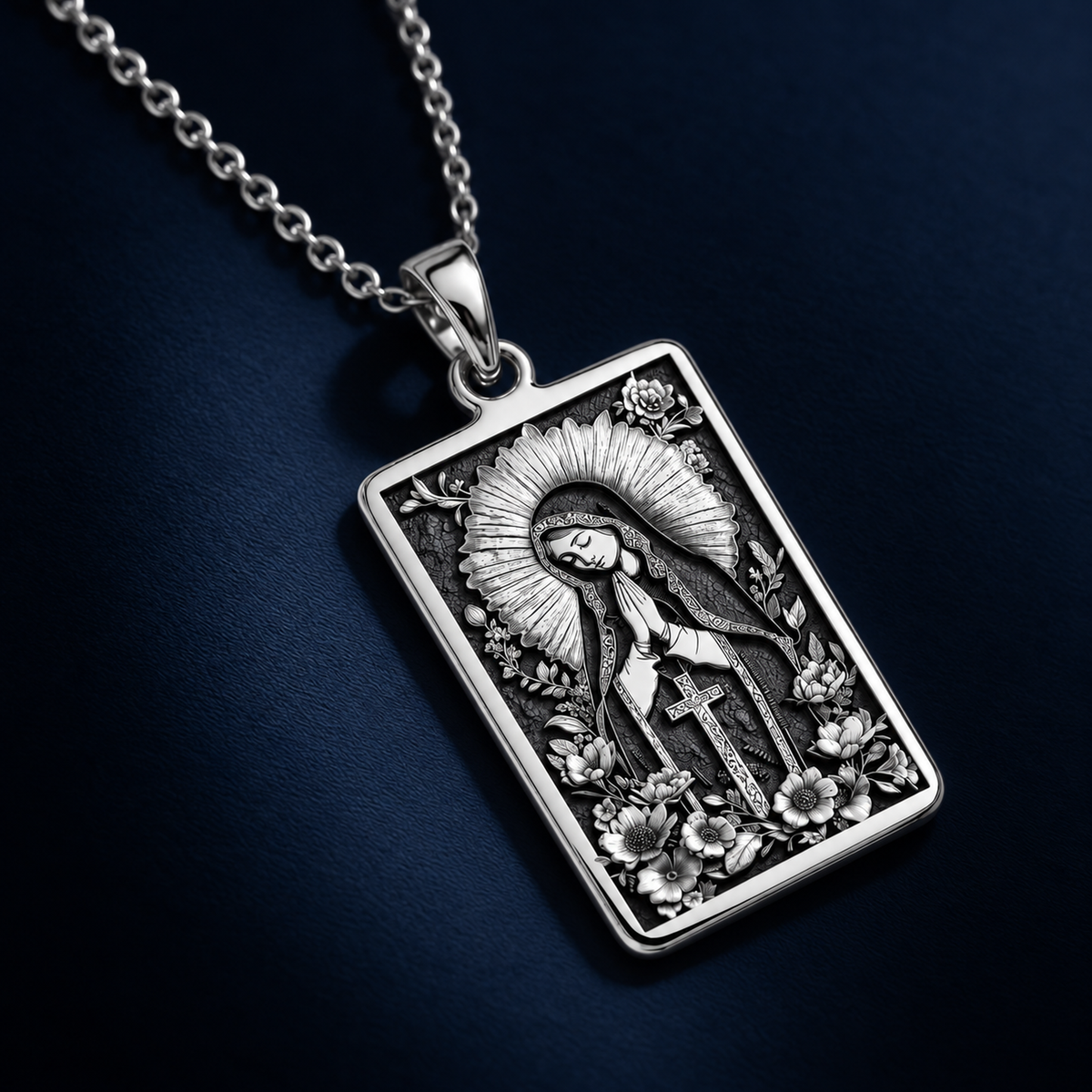 Silver plated rectangular pendant necklace featuring an ornate design of a figure framed by floral elements. The pendant is attached to a silver-toned chain and displayed on a black velvet background with scattered gemstones.