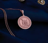 Rose gold plated Buddha pendant necklace showcasing a peaceful meditation scene. This circular medallion features beautifully detailed engravings of Buddha in restful contemplation, head gently resting on hand. The warm rose gold plating creates an elegant contrast with the antique finish of the intricate border details, all suspended from a matching chain against soft white fabric.