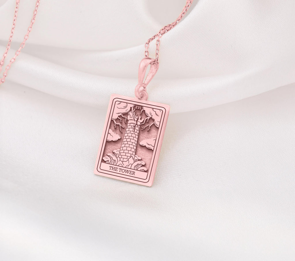 The Tower tarot card rose gold boho chic pendant necklace , depicted in a striking rose gold color features a tall, imposing structure being struck by highlighting the crumbling tower as it tilts precariously. Two figures are shown falling from the structure, symbolizing sudden upheaval or chaos. The background is often minimal, allowing the vivid rose gold tones to emphasize the tower's destruction and the sense of unexpected change or revelation it represents.
