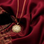 A hand displays a silver toned square geometric pendant necklace. The pendant features detailed internal patterns and hangs from a silver chain, resting on dark fabric.
