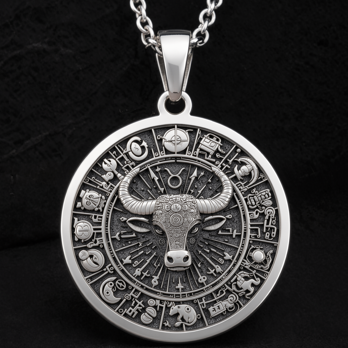 Silver pendant necklace featuring a circular Taurus bull zodiac design with intricate details and a textured surface finish. The necklace is displayed on a dark green velvet fabric with warm string lights in the background.