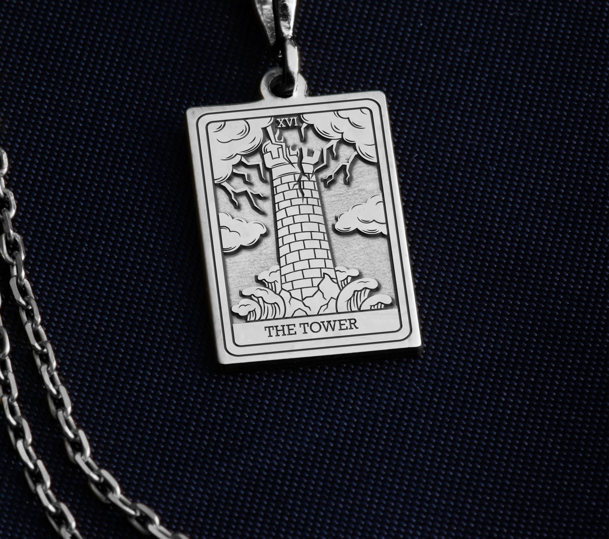 The Tower tarot card silver boho chic pendant necklace , depicted in a striking silver color features a tall, imposing structure being struck by highlighting the crumbling tower as it tilts precariously. Two figures are shown falling from the structure, symbolizing sudden upheaval or chaos. The background is often minimal, allowing the vivid silver tones to emphasize the tower's destruction and the sense of unexpected change or revelation it represents.