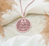 Buddha figure seated in meditative lotus pose (Padmasana) upon a blooming lotus flower base. The trendy, warm pinkish hue of the durable rose gold plating [over Specify Base Metal if Known] enhances the detailed artistry of the central deity and the surrounding ornate floral mandala-style patterns filling the circular frame.Perfect yoga or mindfulness fashion jewelry gift.