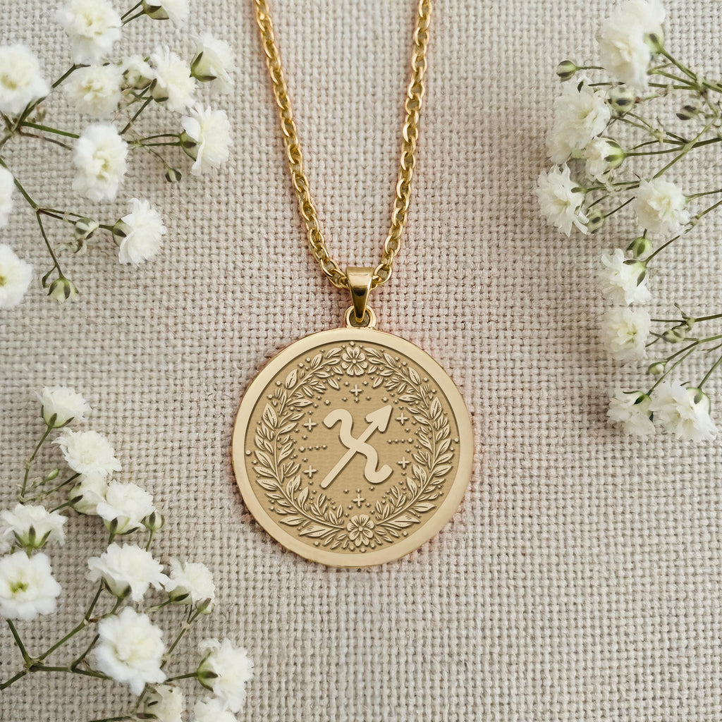 Customizable 14K Solid Gold Sagittarius Necklace on a satin background. The zodiac pendant is framed by a laurel wreath and can be engraved, making it a unique spiritual birthday gift