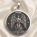 Silver pendant necklace featuring a detailed design of a winged figure with outstretched wings in a circular frame. The surface has a matte finish and is displayed on a delicate silver chain.