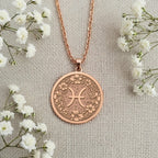 Engravable Rose Gold Plated Pisces Pendant on a textured surface. The floral horoscope symbol medallion is a perfect personalized gift for a March or February birthday. Customizable jewelry.