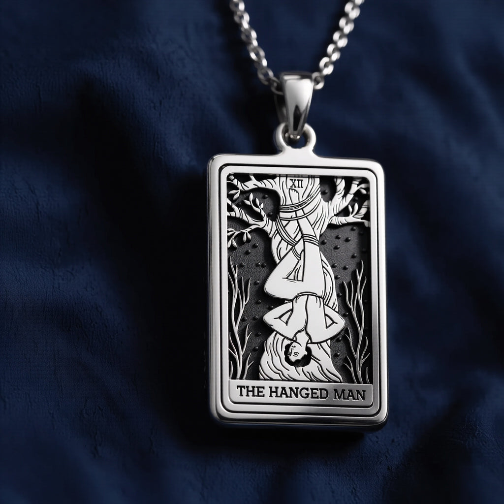 Rectangular sterling silver pendant featuring an engraved depiction of The Hanged Man tarot card with Roman numeral XII, suspended on a chain against dark fabric.