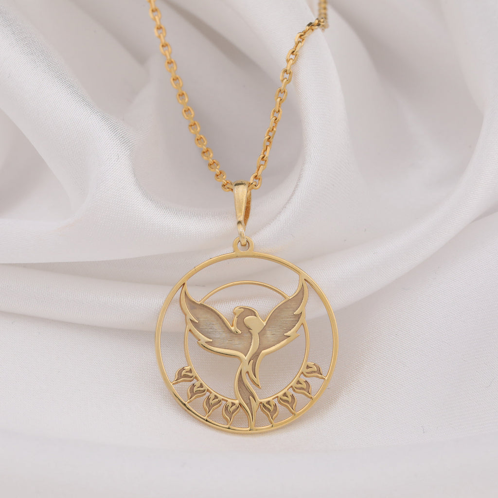 Phoenix Rising Necklace: 14K gold pendant showing a front view of a rising phoenix within a circular frame and leaf accents.