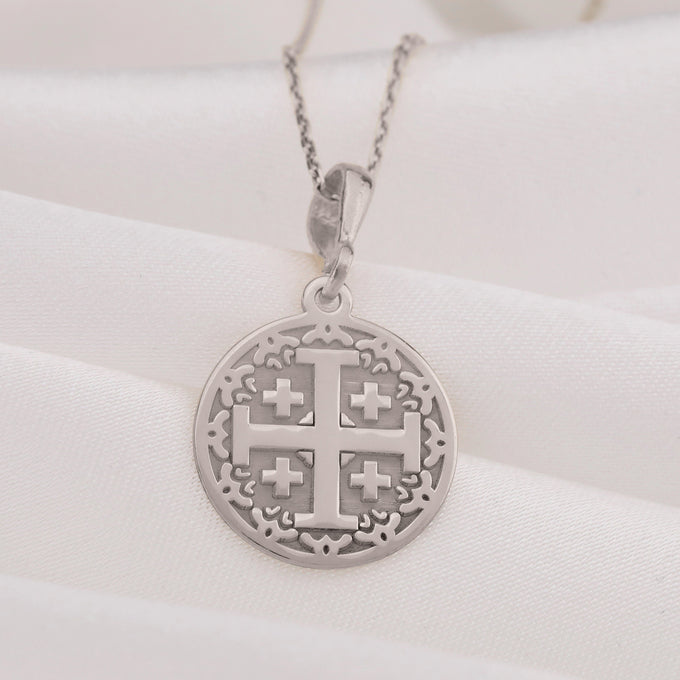 Silver Jerusalem Cross pendant with detailed geometric design and an engraved border. A silver chain is visible beneath the pendant, set against a white background.