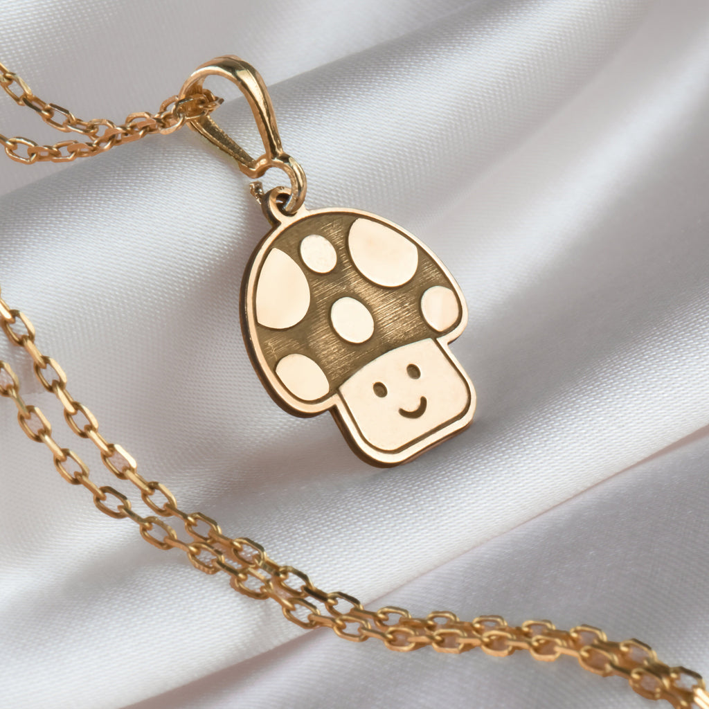 Magic Mushroom Amulet Pendant Necklaces 14K 14K Gold Plated mushroom pendant with a smiling face necklace on white fabric.