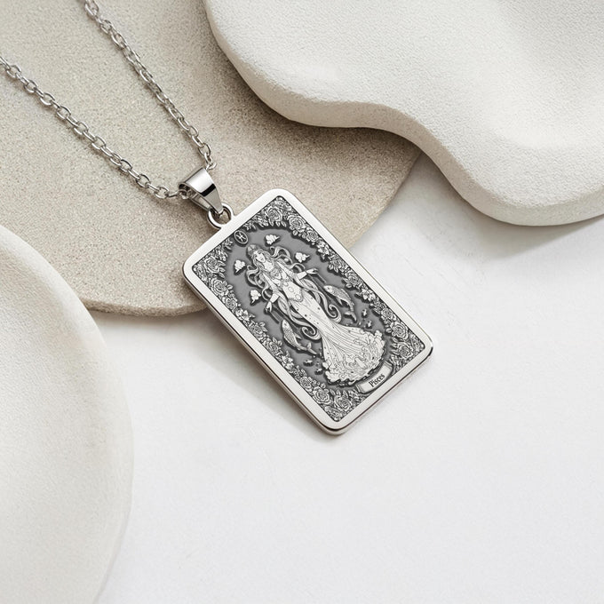 Silver plated rectangular pendant with fine detailing of a classical figure within an elaborate border. The necklace features a silver chain and is presented against a soft background.