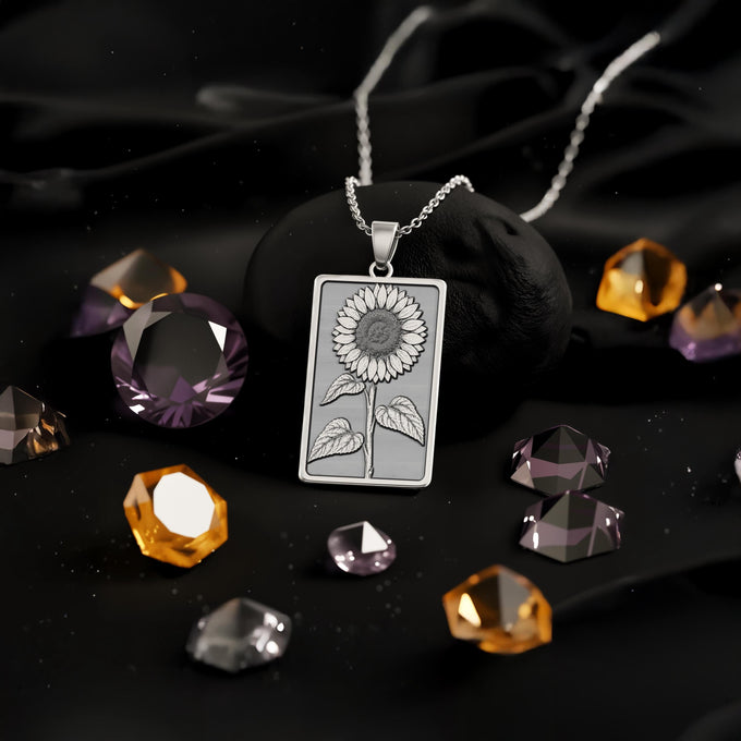 Silver rectangular pendant featuring an etched outline of a sunflower and leaves. This piece is attached to a silver colored chain, viewed directly from above.
