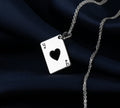 A silver pendant necklace featuring a heart shape with a queen of hearts motif, set against a dark blue fabric background. The pendant has a polished finish and is attached to a delicate silver chain.