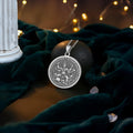 Silver circular pendant featuring an intricate design of a goddess surrounded by skulls and faces. The pendant is attached to a silver-toned chain and displayed on a dark background.
